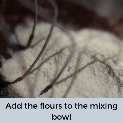flour added to gluten and dairy free brownie batter in a mixing bowl with a whisk attachment