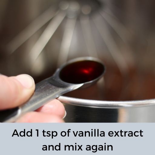 hand holding a tsp of vanilla above a stainless steel mixing bowl